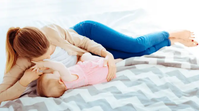 Young mother lying in bed breastfeeding her baby
