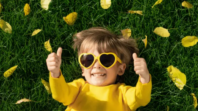 Smiling child in a yellow top lying on the grass with arms raised