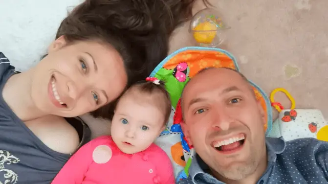 Young family with a baby lying on the ground and smiling at the camera