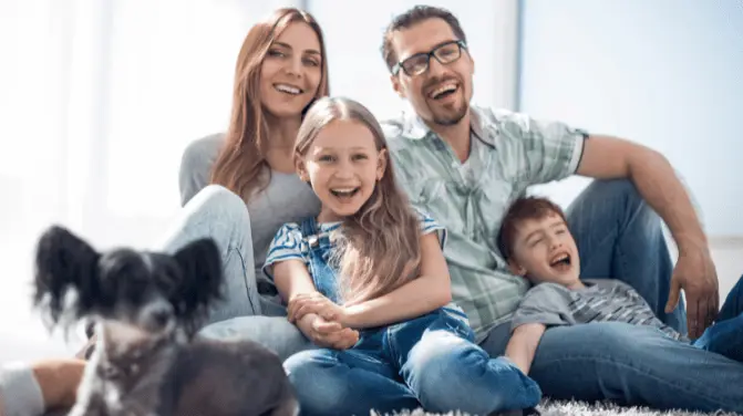 A happy family with two children and a dog, smiling, sitting on a sofa