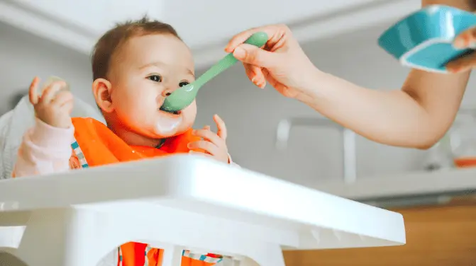 Baby in a highchair eating from a blue bowl with a spoon